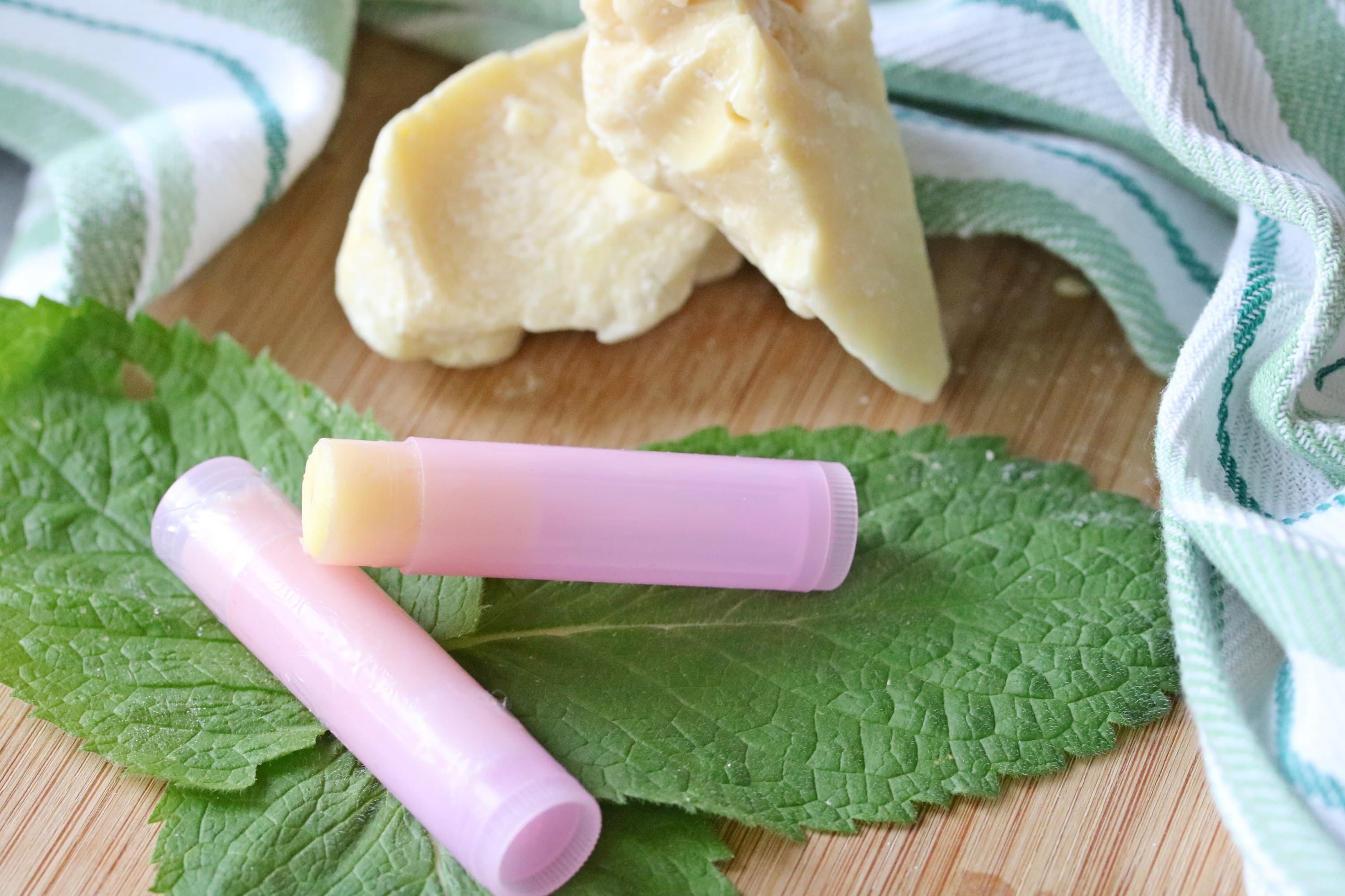 Diy lip chap in purple tubes on green mint leaves with cacao butter behind them