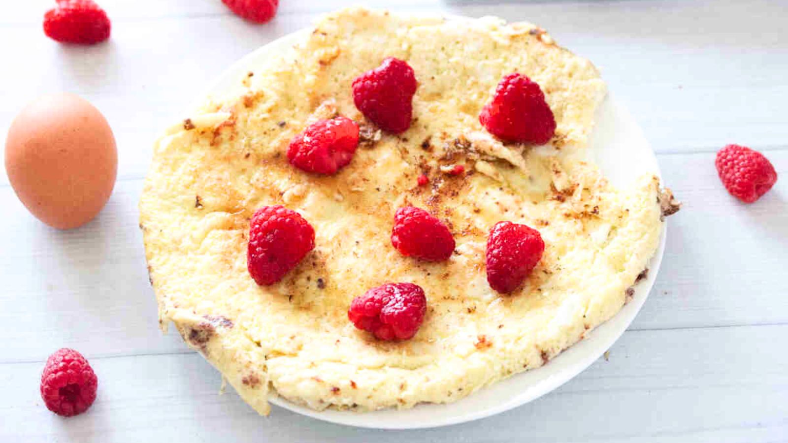 Egg white protein pancake on a white plate with raspberries on top.