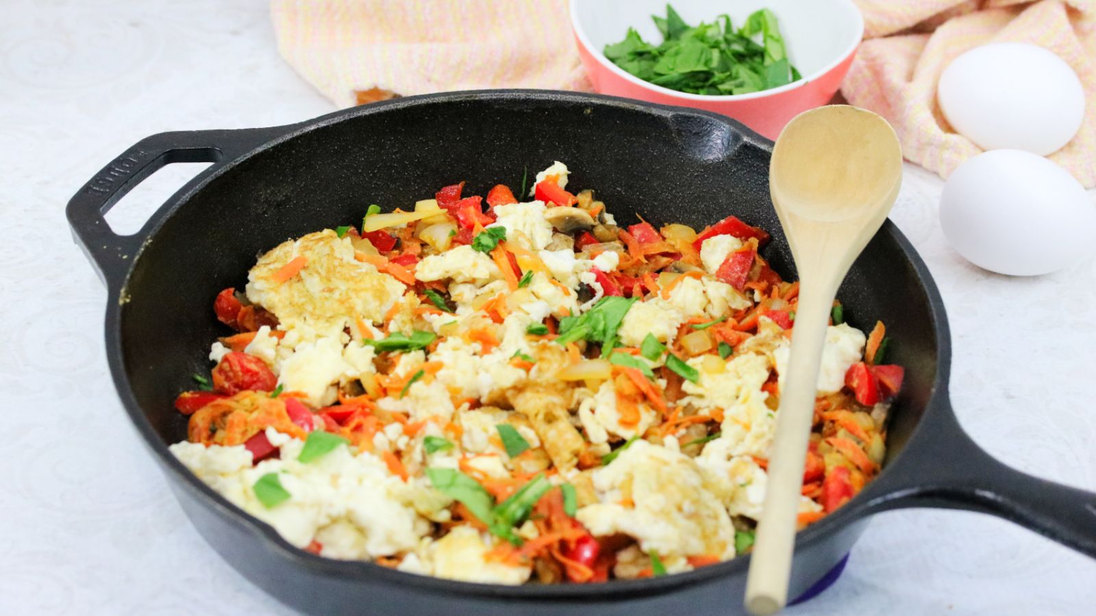 Healthy egg scramble with carrots, green onion, and peppers in a cast iron skillet.