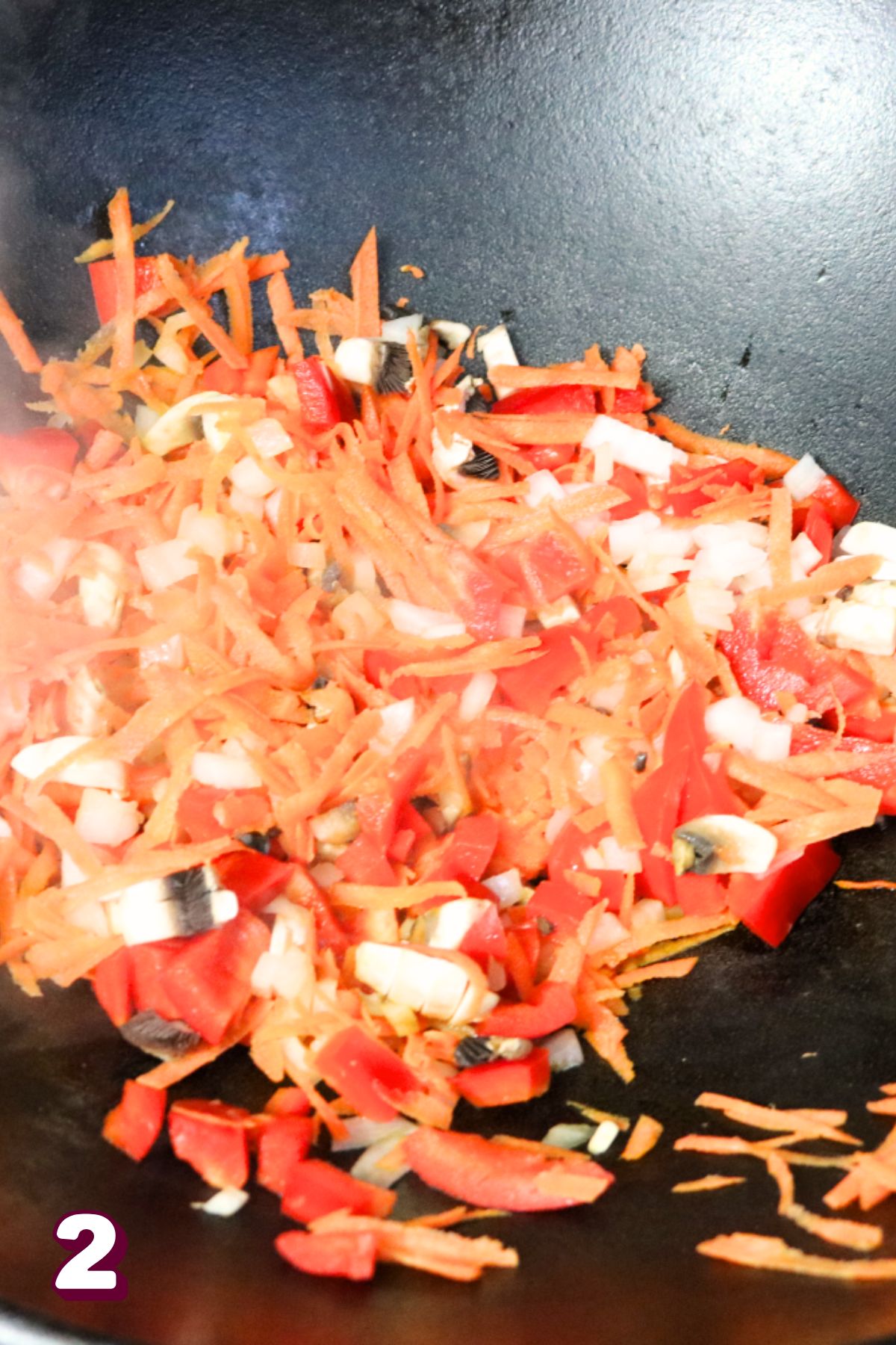 Cast iron skillet with peppers and carrots cooking in it.