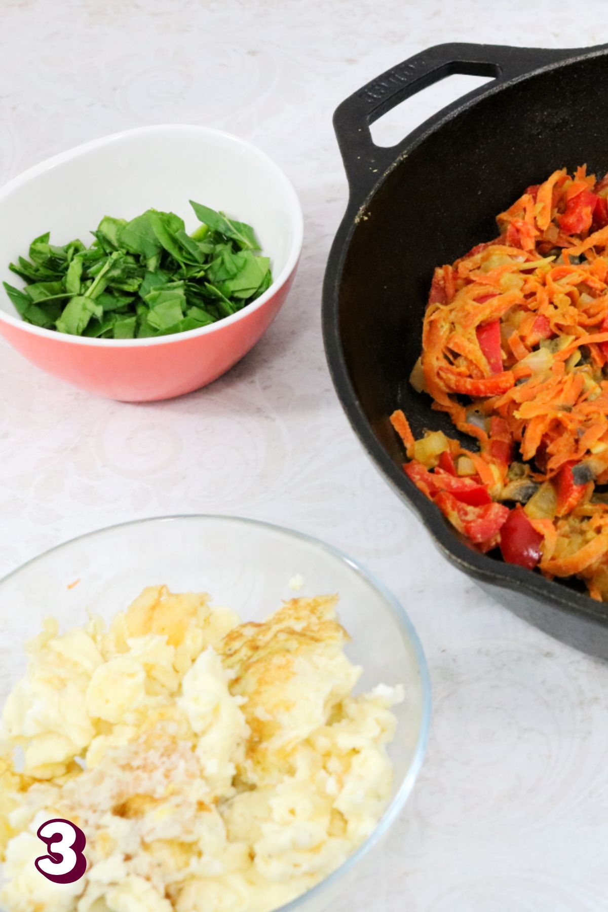Cast iron skillet of vegetables with scrambled eggs and spinach beside it.
