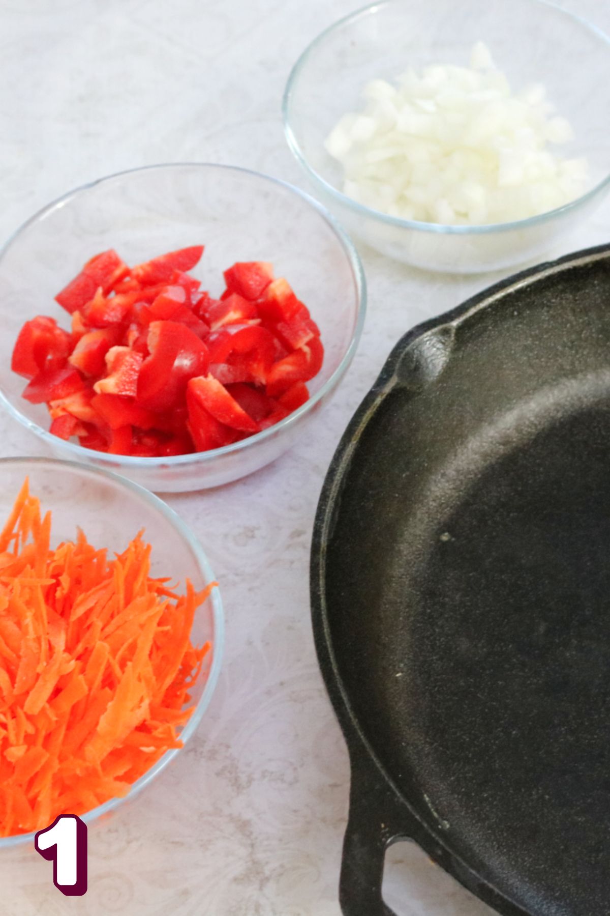 Cast iron skillet with glass bowls of vegetables around it.