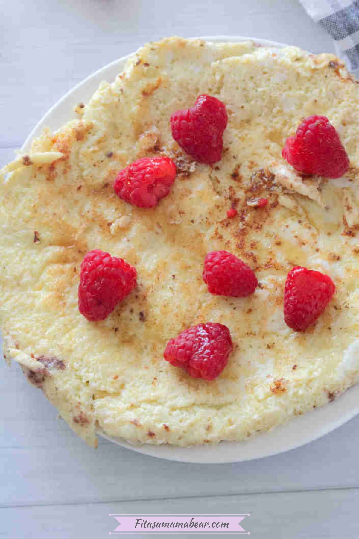 Egg white protein pancake on a white plate with raspberries on top.
