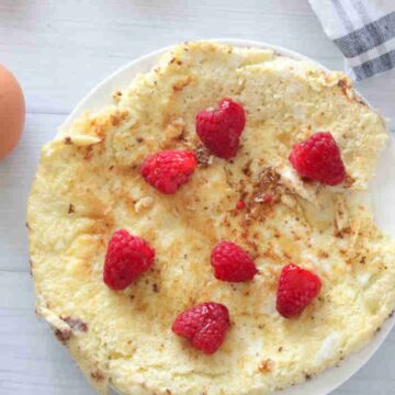 Egg white protein pancake on a white plate with raspberries on top.