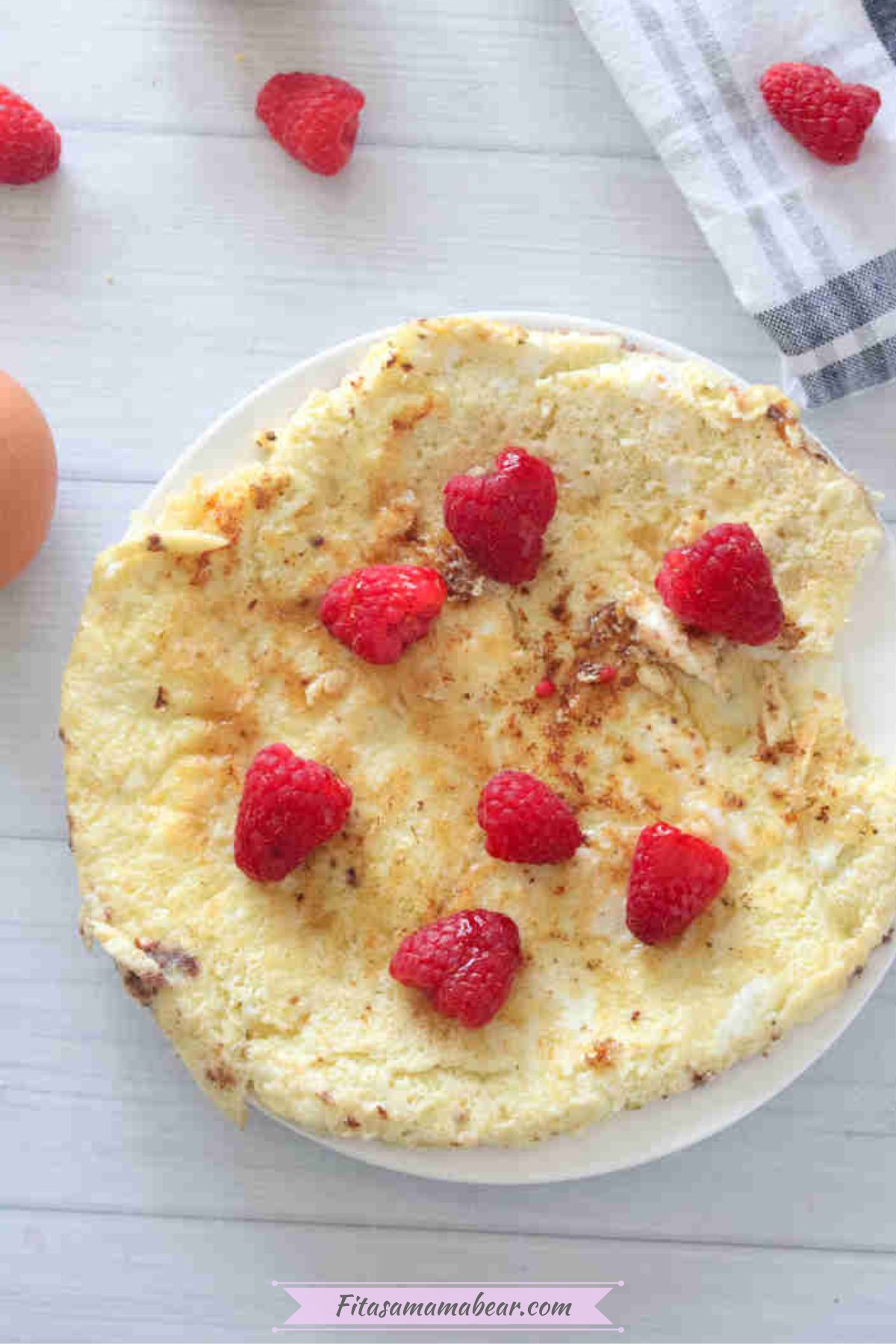 Egg white protein pancake on a white plate with raspberries on top.