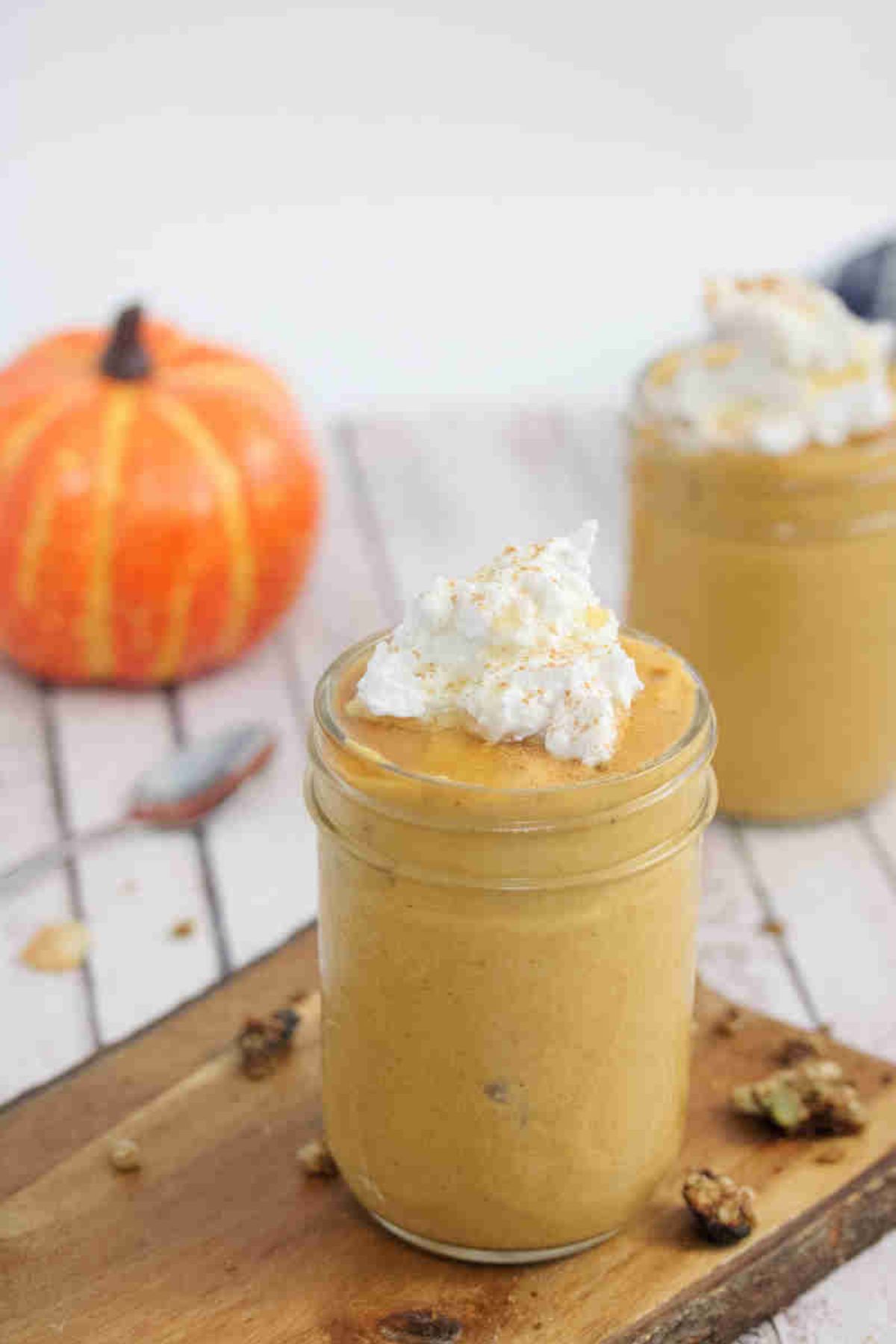Pumpkin smoothie topped with coconut whipped cream in a mason jar on a wooden cutting board.
