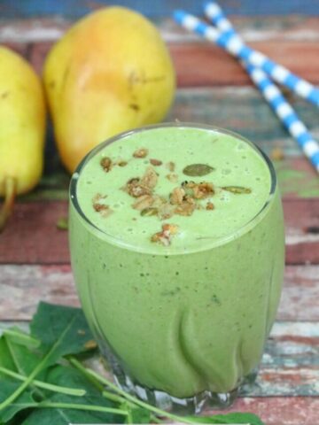 Green smoothie in a glass with granola on top and spinach, blue straws, and pears around it.