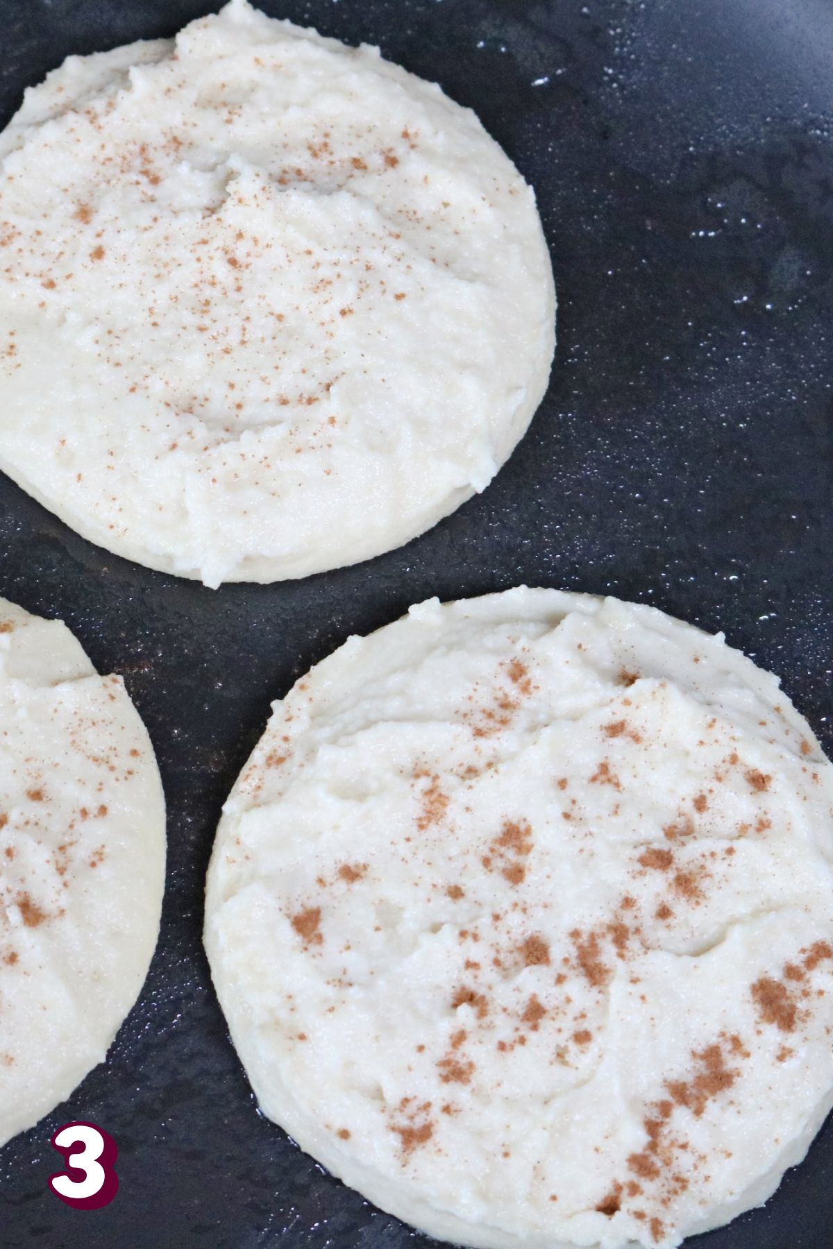 Three circles of raw pancakes in a black pan.