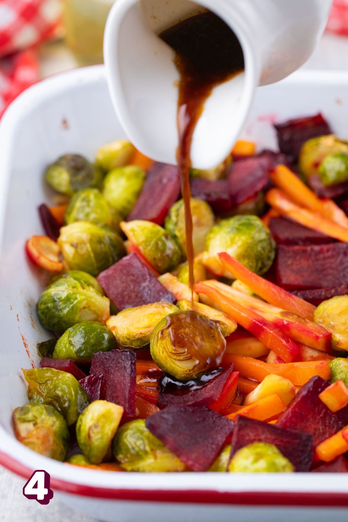 Brussels, carrots, turnips, and beets in a baking dish with dressing being poured.