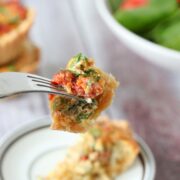 Mini quiche on fork with quiche on a plate and stacked behind it.