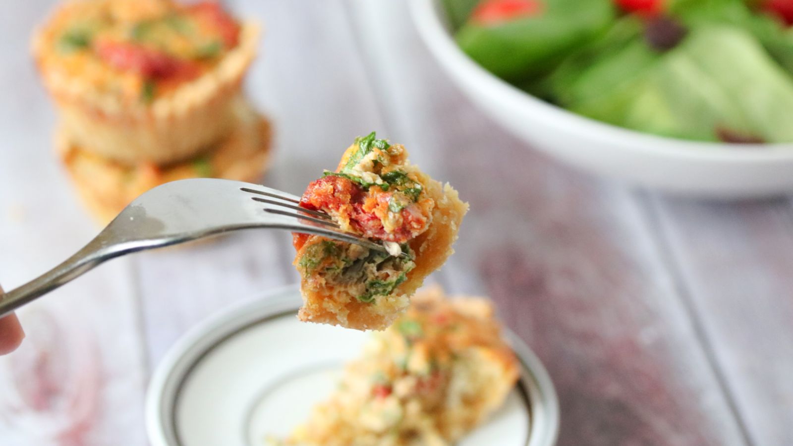 Mini quiche on fork with quiche on a plate and stacked behind it