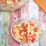 Glass bowl with chickpeas, quinoa, red pepper, and tomatoes with more quinoa salad behind it.