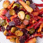 Roasted carrots, beets and Brussels sprouts on white plate with sesame seeds.