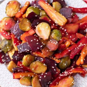 Roasted carrots, beets and Brussels sprouts on white plate with sesame seeds.