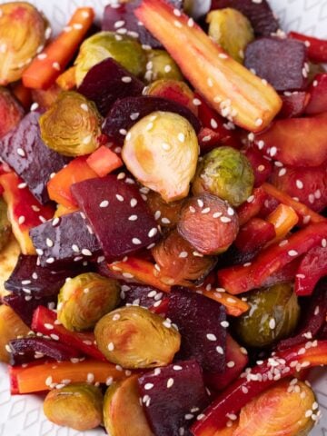 Roasted carrots, beets and Brussels sprouts on white plate with sesame seeds.