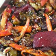 Roasted carrots, beets and Brussels sprouts on a tinfoil lined pan topped with sesame seeds.