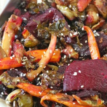 Roasted carrots, beets and Brussels sprouts on a tinfoil lined pan topped with sesame seeds.