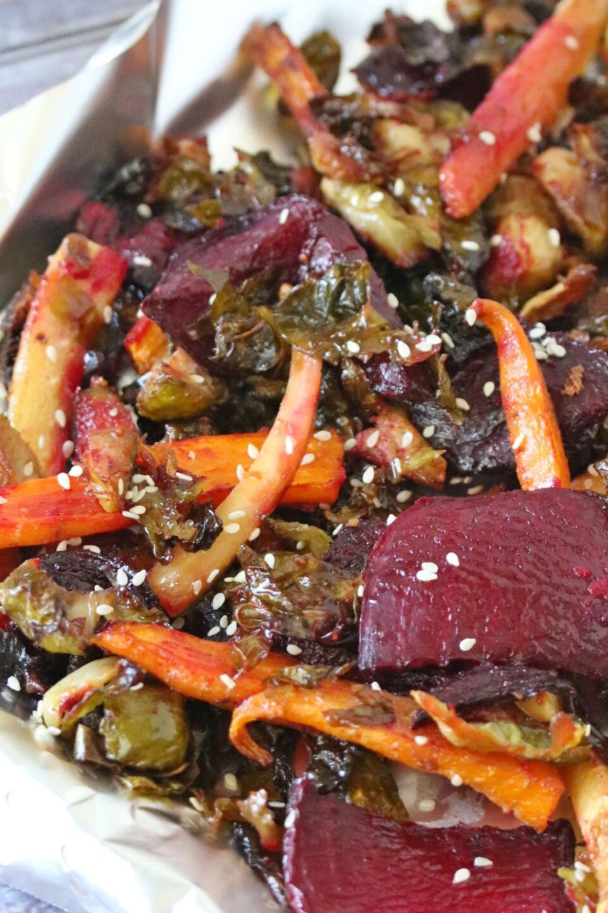 Roasted carrots, beets and Brussels sprouts on a tinfoil lined pan topped with sesame seeds.