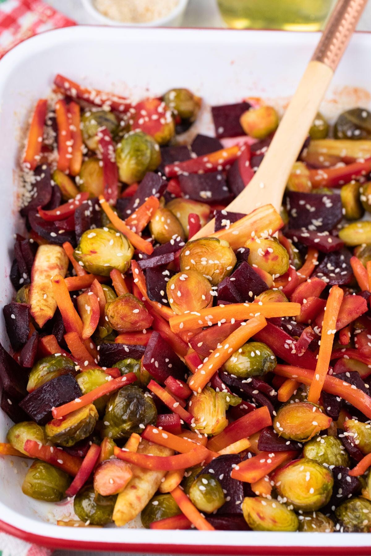Roasted carrots, beets and Brussels sprouts in a baking pan with a spoon in them.