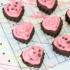 Heart shaped chocolate cupcakes topped with pink icing and chocolate chips on a cooling rack.