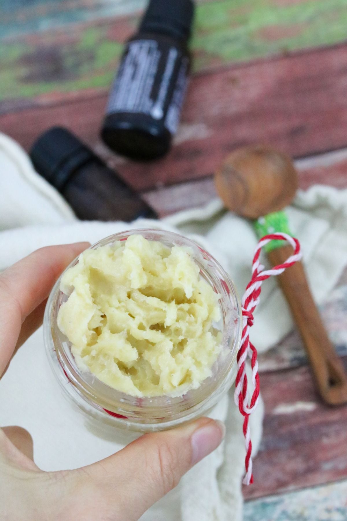 Homemade muscle rub in a glass jar with a red string around it being held by two fingers.