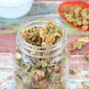 Mason jar with cinnamon granola in it and orange scoop and white ramekin with more granola in it.