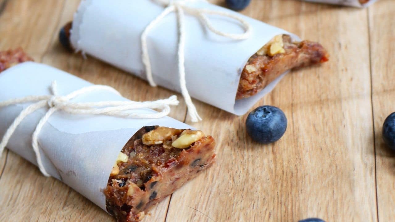 three fruit and nut bars wrapped in parchment paper with blueberries around it