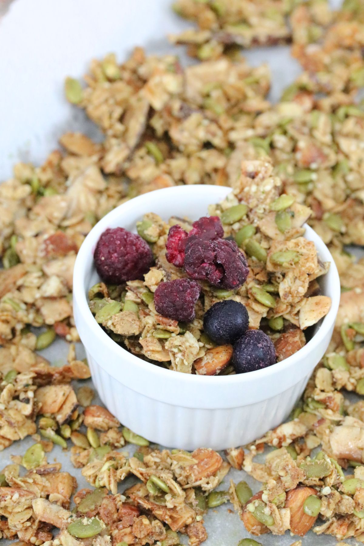 White ramekin with crunchy vegan granola in it and granola around it.