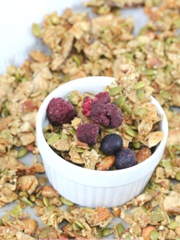 White ramekin with crunchy vegan granola in it and granola around it.
