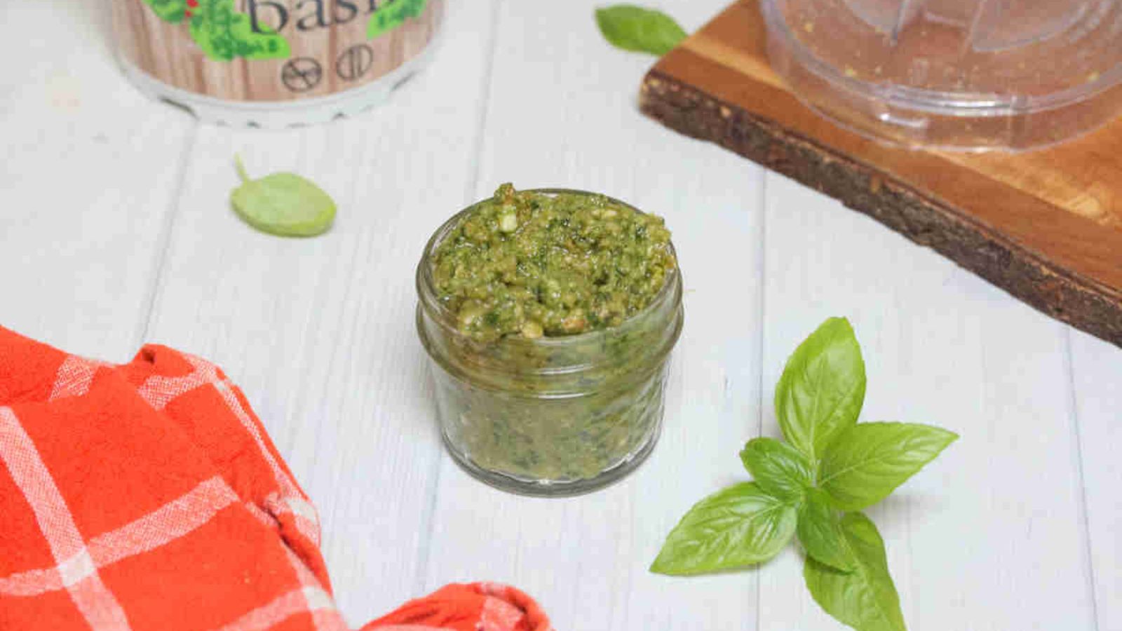 Dairy-free pesto sauce in a mason jar with basil leaves and a plant around it.