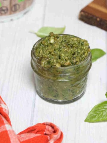Dairy-free pesto sauce in a mason jar with basil leaves and a plant around it.