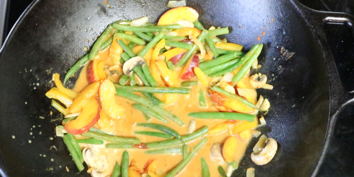 Green beans, peaches, onions, and garlic, in a coconut milk broth in a cast iron pan.