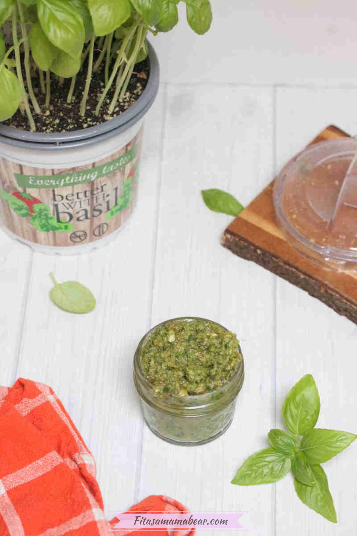 Dairy-free pesto sauce in a mason jar with basil leaves and a plant around it.