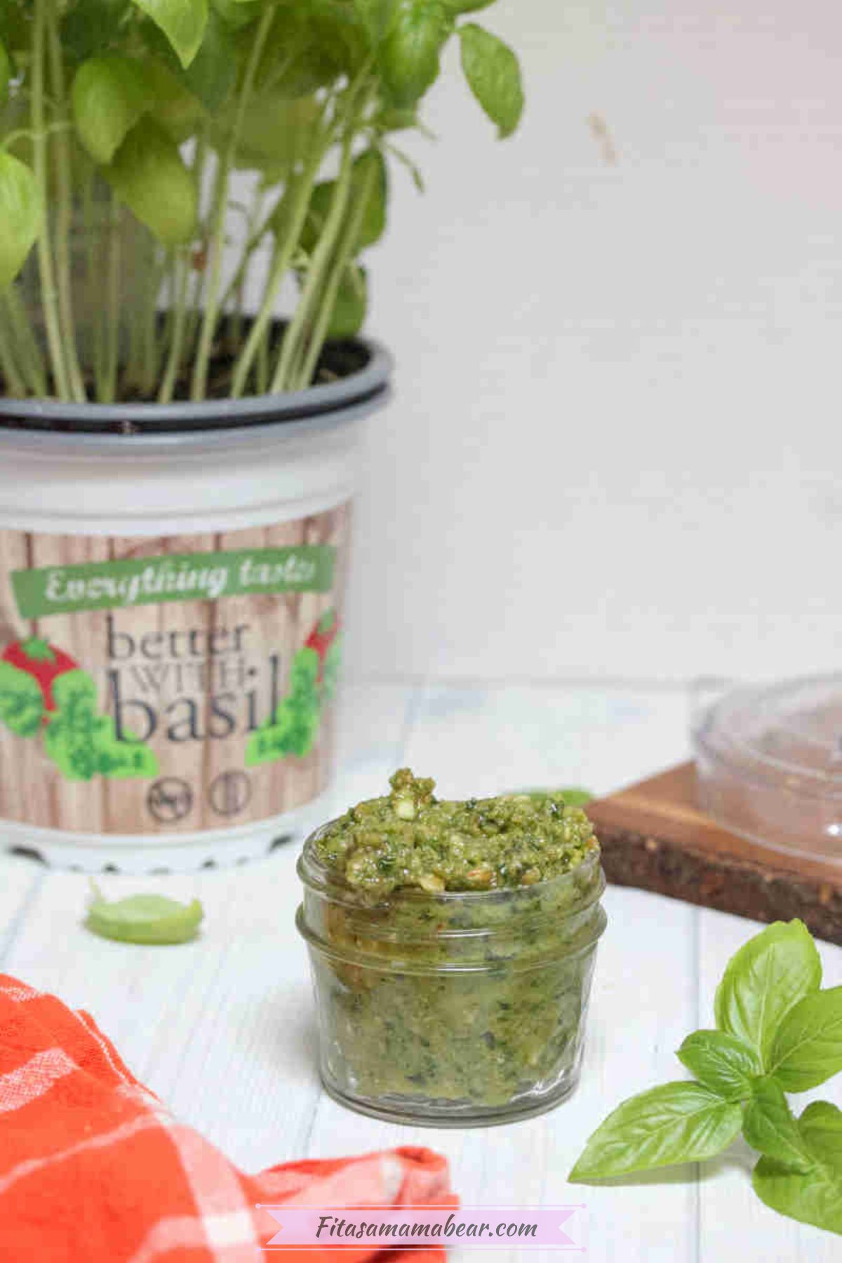Dairy-free pesto sauce in a mason jar with basil leaves and a plant around it.