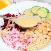 Beet, cucumber, radish, and chickpeas on top of quinoa in a white bowl and a spoon over it with dressing.