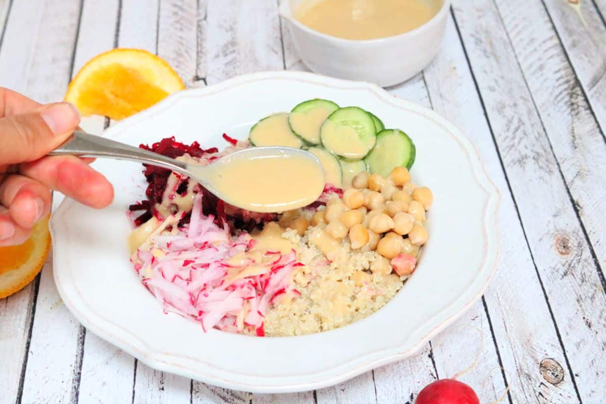 Beet, cucumber, radish, and chickpeas on top of quinoa in a white bowl and a spoon over it with dressing.