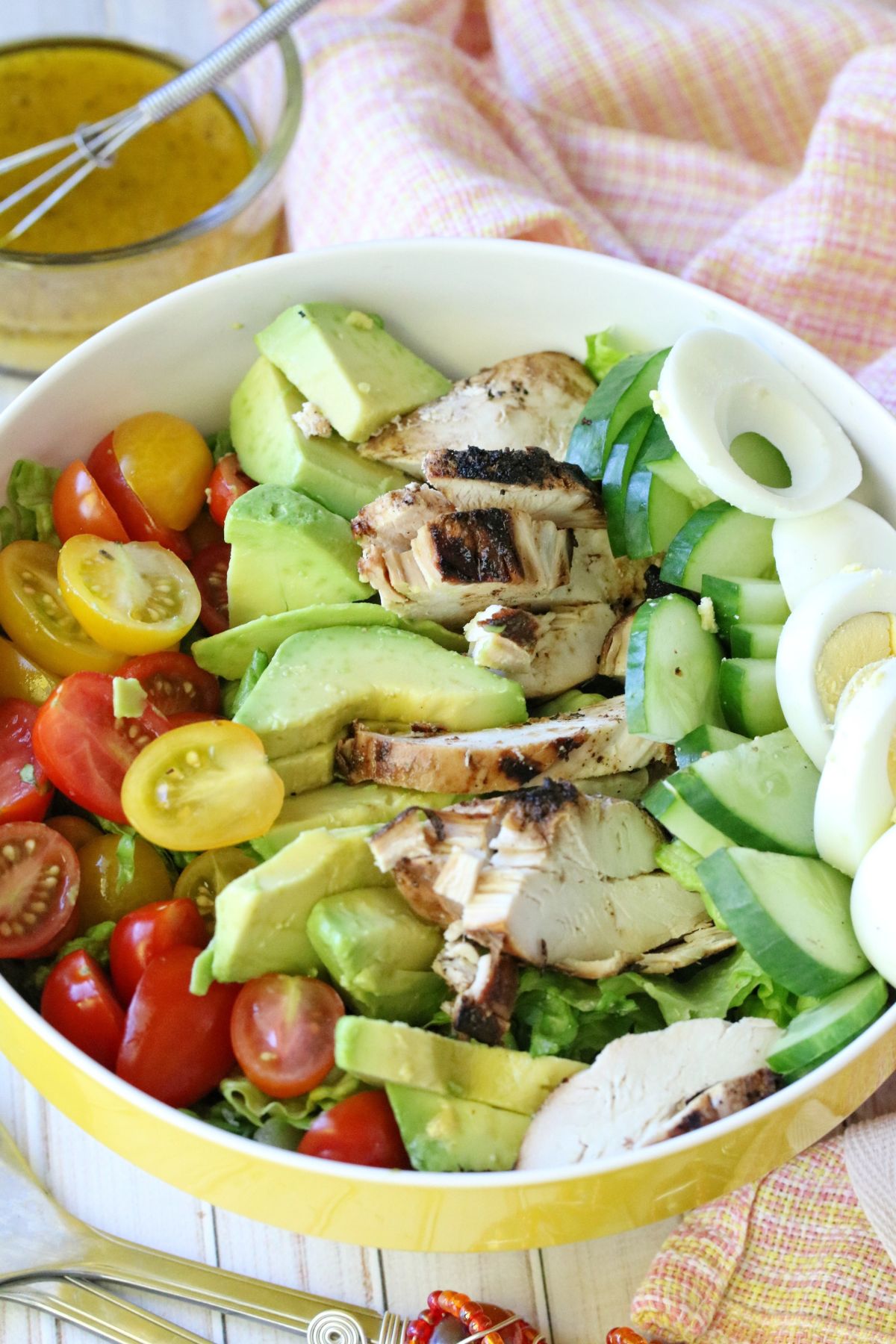 Dairy-free cobb salad in a large yellow mixing bowl with a peach napkin and a measuring cup of dressing behind it.