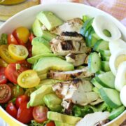 whole30 cobb salad in a large yellow mixing bowl with a peach napkin and a measuring cup of dressing behind it