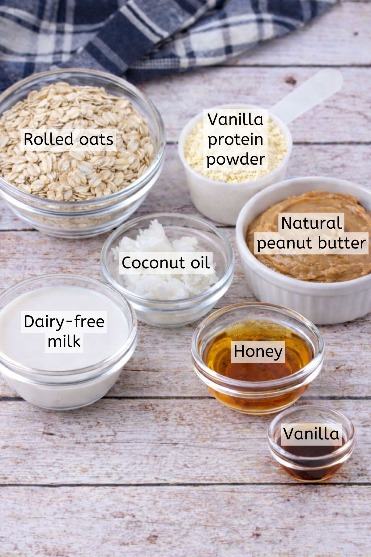 Peanut butter, protein powder, oats, honey, and maple syrup in bowls with text labels over top.