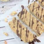 Five peanut butter vanilla protein bars lined up flat on parchment paper and drizzled with chocolate.