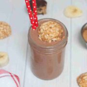 Chocolate peanut butter cup smoothie in mason jar topped with peanut butter bomb in it and red straws in it.