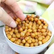 White bowl with roasted chickpeas in it and a hand grabbing them.