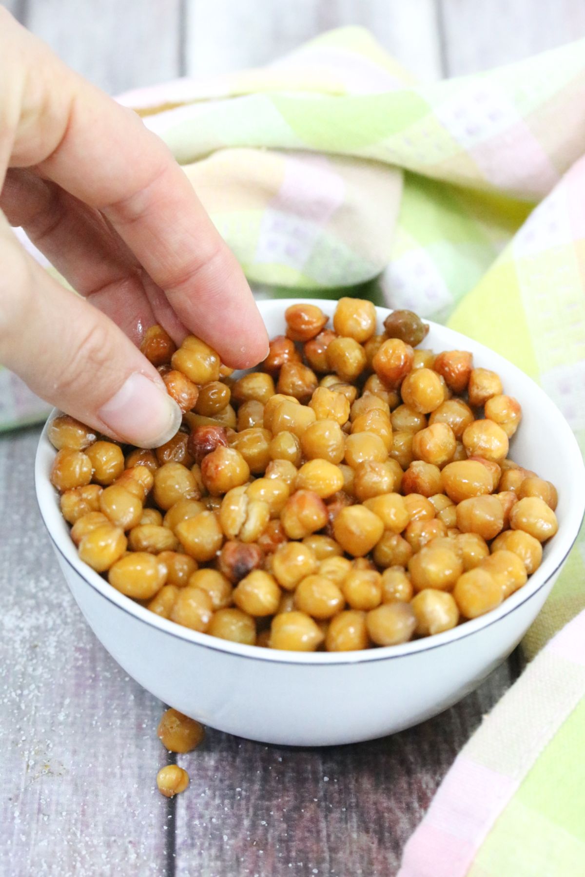 White bowl with roasted chickpeas in it and a hand grabbing them.