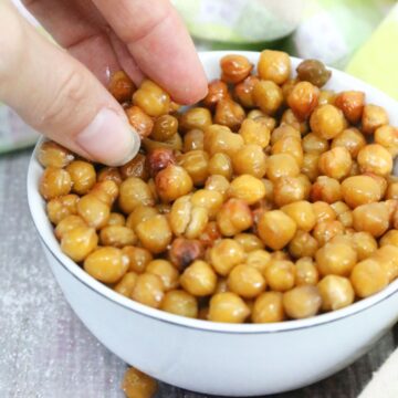 White bowl with roasted chickpeas in it and a hand grabbing them.