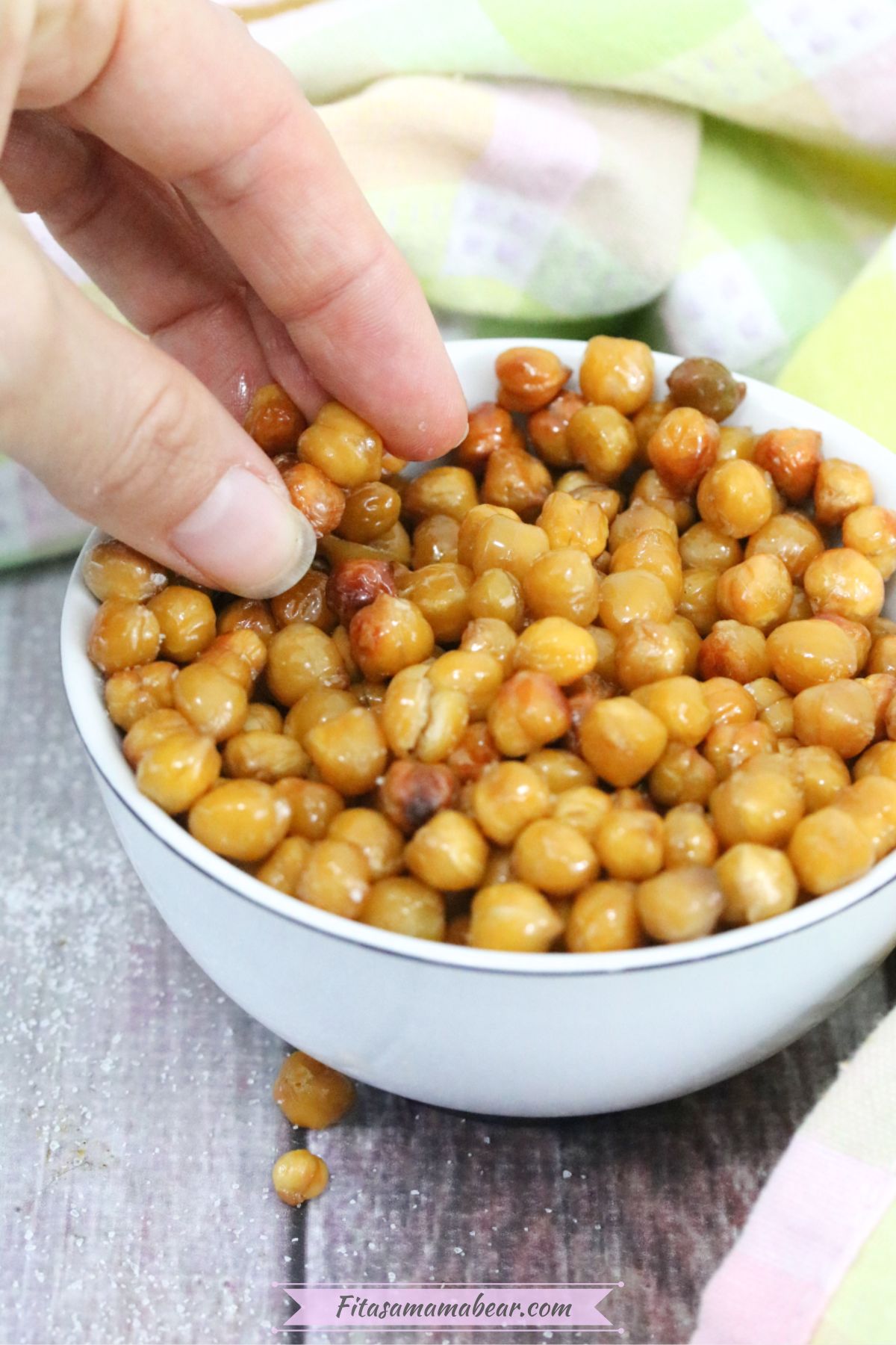 White bowl with roasted chickpeas in it and a hand grabbing them.