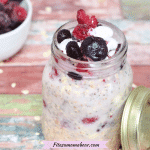 Dairy-free overnight oats in a mason jar topped with frozen berries and coconut whip cream with the jar lid beside it and a bowl of berries behind it
