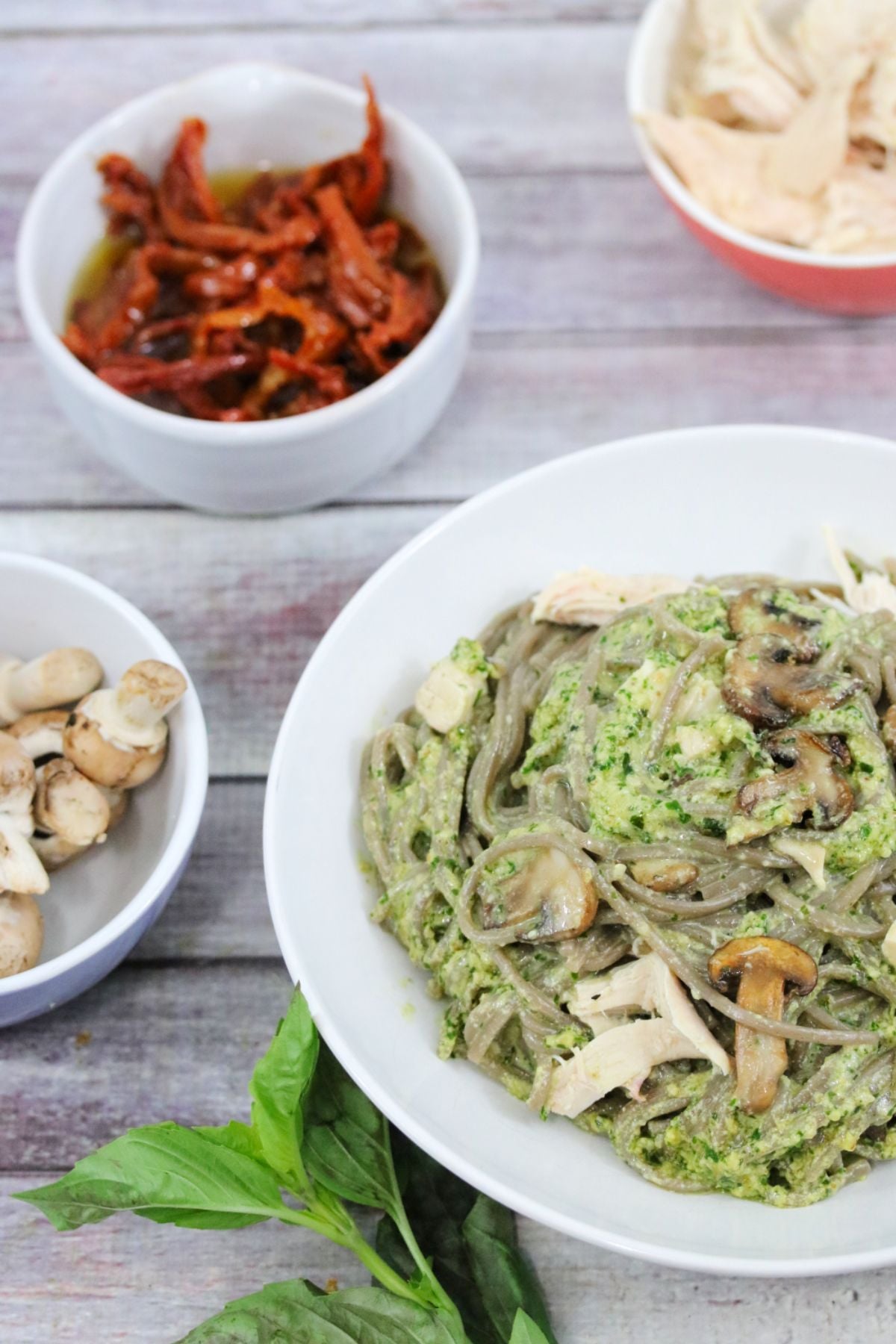 Creamy pesto pasta in a white bowl with ingredients around it.