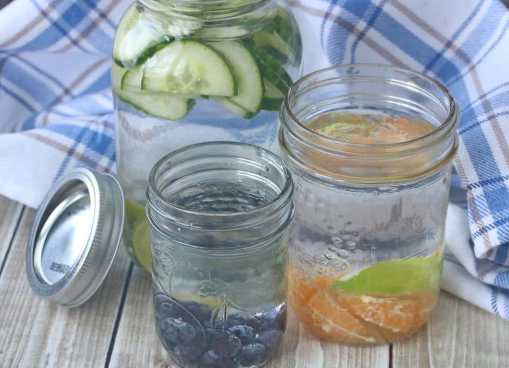 Three mason jars with fruit and water in them with a blue napkin behind them