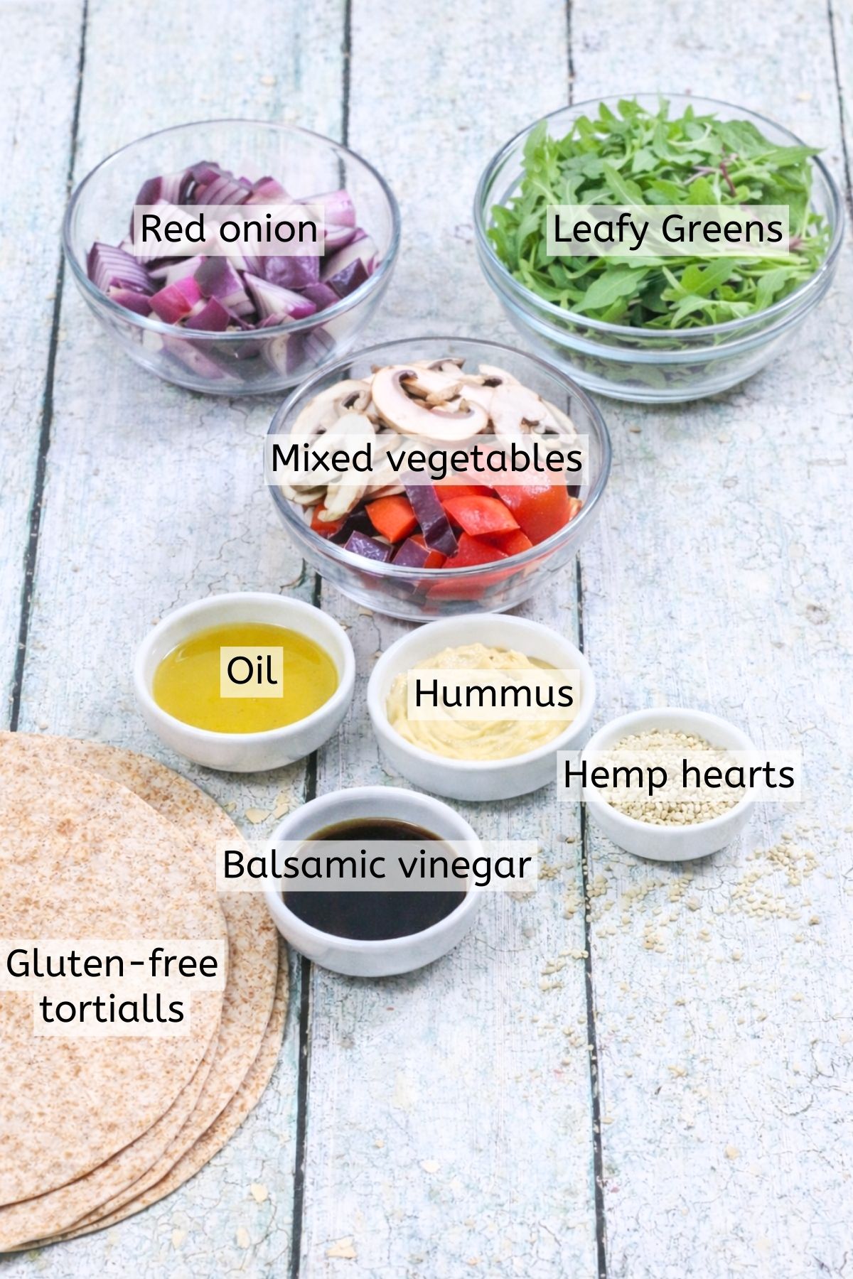 Hummus, vegetables, oil, and balsamic vinegar in bowls with text labels over top.