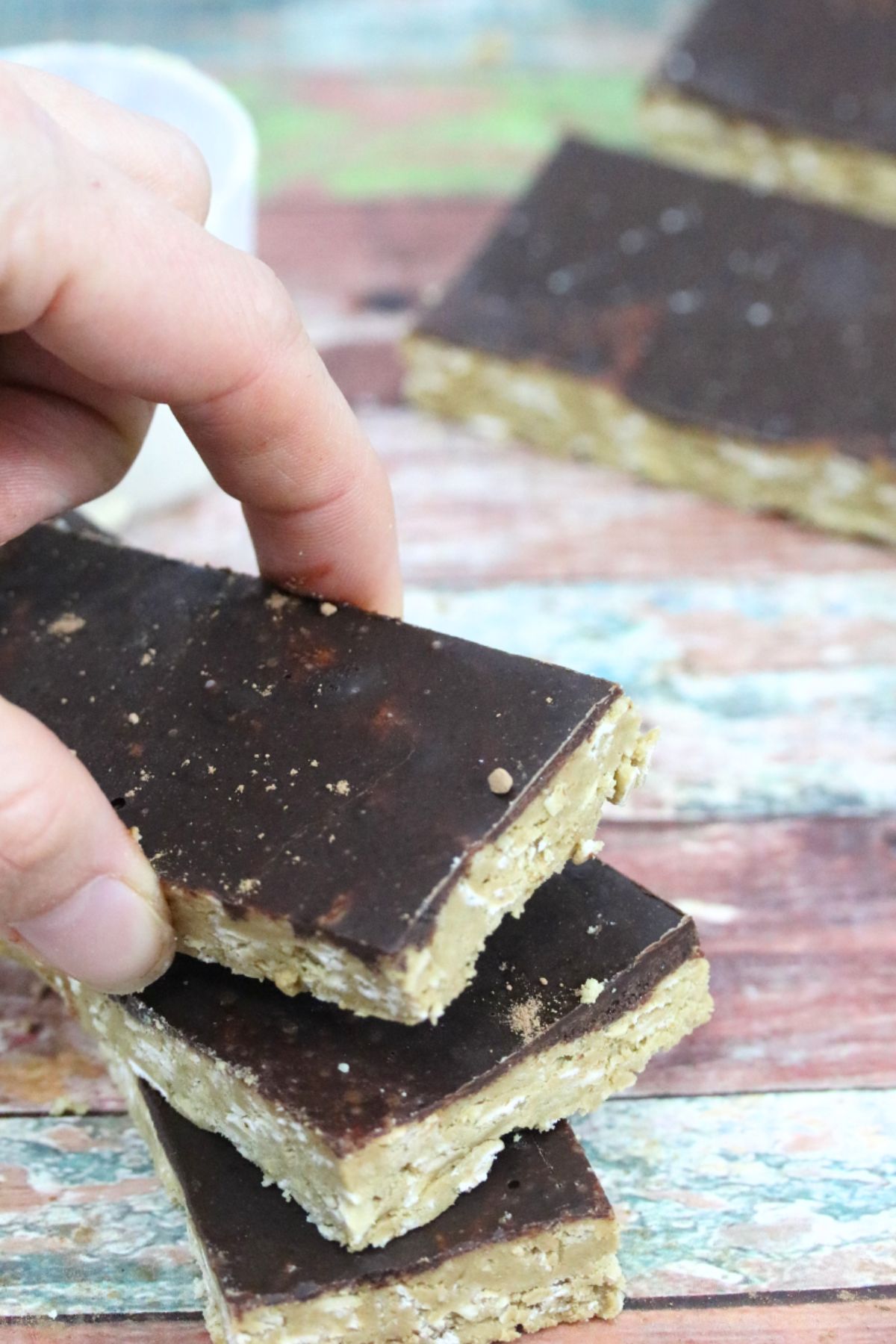 Three homemade protein bars with chocolate on top stacked with a hand placing the last one on top.